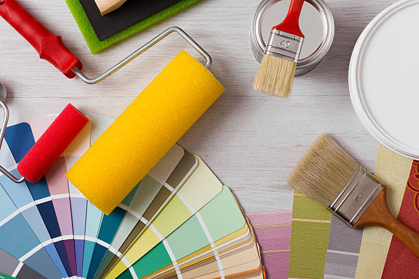 Painter and decorator work table with house project, color swatches, painting roller and paint brushes, top view