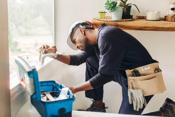 African male plumber looking at leaking bathroom tap. Professional handyman trying to fix a bathroom faucet.